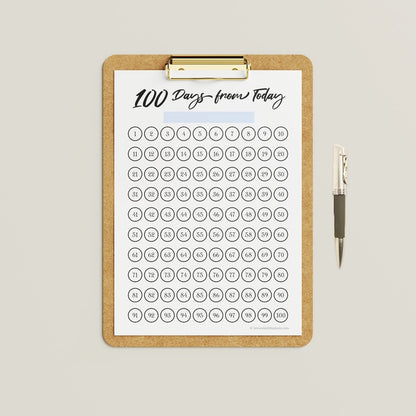 Mockup showing an example of use for the black and white version of the '100 Days from Today' printable 100-day challenge calendar, which can be colored in by hand.
